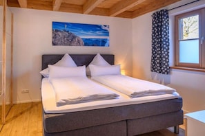 A double bed with a dark headboard, a painting of a mountain landscape, and a window with star-patterned curtains.