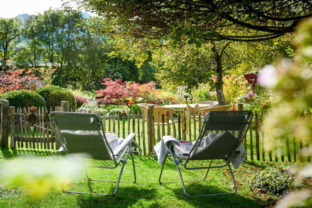 A garden with two lawn chairs, a wooden fence, and various plants.