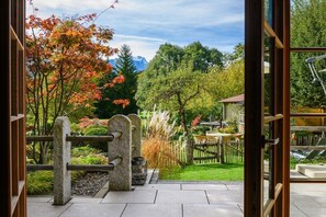 A view through a wooden gate into a garden with a stone fence, a lawn, and a mountain in the background.