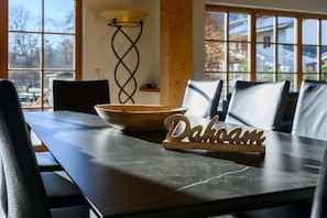 A dining table with a wooden bowl and a sign reading 'Dakoam' in a room with large windows and a tall floor lamp.