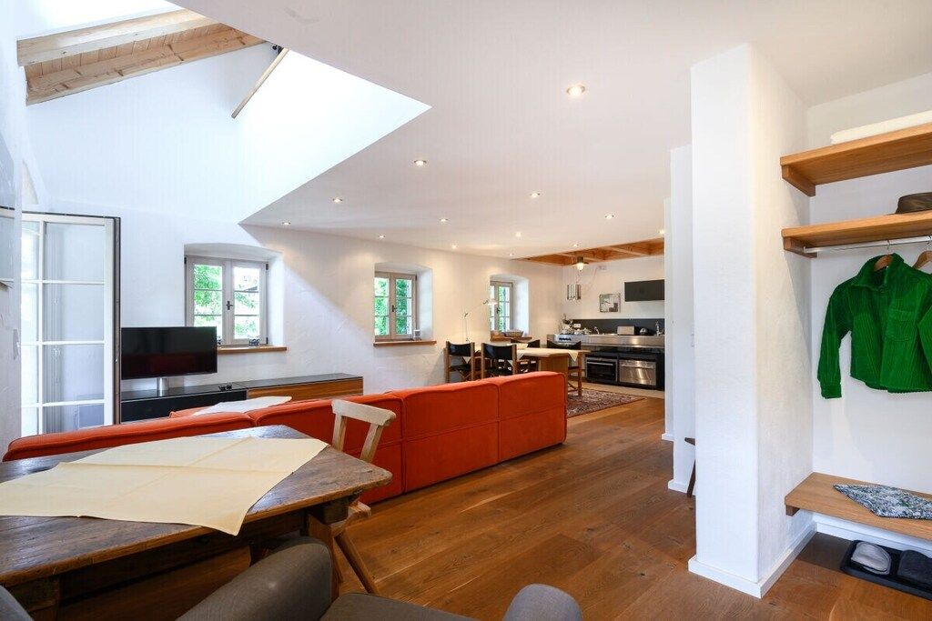 A modern living space with a dining area, a kitchen, and a seating area with a red sofa.