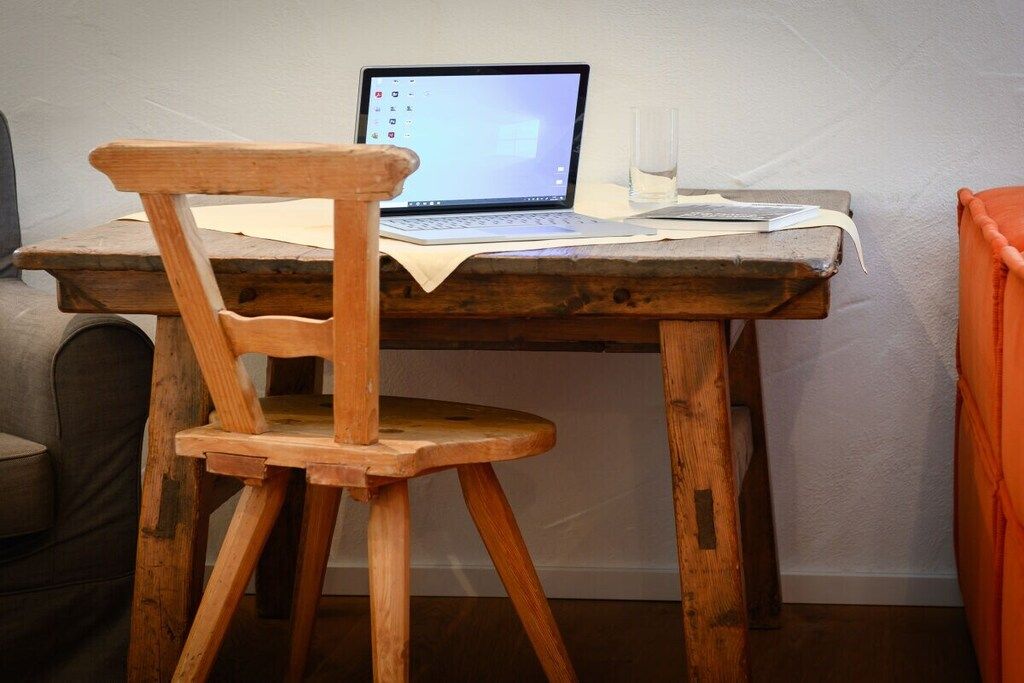 A wooden chair with a laptop on a rustic wooden table.