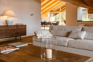 Un salon moderne avec un plafond en bois, un canapé, une table en verre avec une bougie et une lampe.
