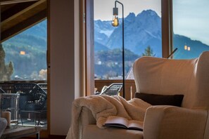 A cozy room with a large window overlooking mountains, a comfortable chair with a book, and a modern floor lamp. - Holiday apartment with 3 bedrooms (Garmisch-Partenkirchen)
