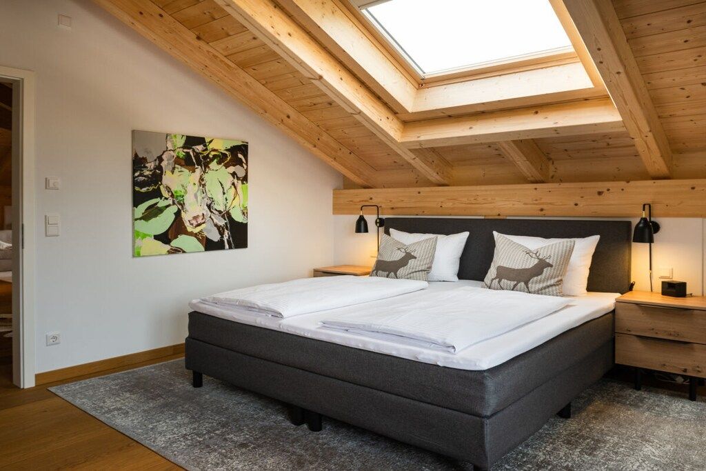 Un dormitorio con tragaluz, una cama con almohadas, una mesita de noche y un cuadro en la pared.