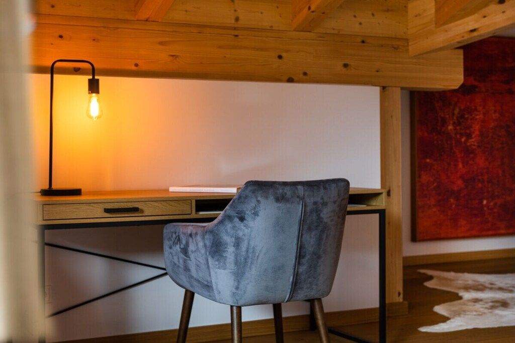 Una camera moderna con soffitto in legno, una scrivania con lampada, una sedia e un quadro astratto rosso appeso al muro.
