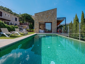 Ein Pool mit Steinverkleidung und Glastür, umgeben von Liegestühlen und freiem Blick auf den Himmel.