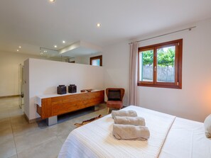 Une chambre à coucher moderne avec un grand lit, une coiffeuse en bois, un miroir et une fenêtre donnant sur un paysage verdoyant.