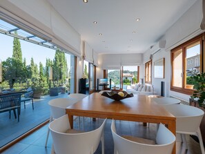 Une salle à manger spacieuse, dotée d’une grande table en bois et de chaises blanches, qui offre une vue magnifique sur le paysage extérieur.