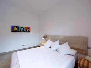 Ein Schlafzimmer mit einem Bett, Kissen, einem Nachttisch mit Lampe und einem Wandbild.
