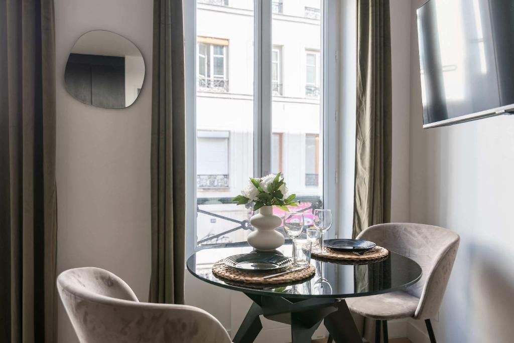 Ein Essbereich mit einem runden Tisch, zwei Stühlen, einer Vase mit Blumen und Blick auf Gebäude.