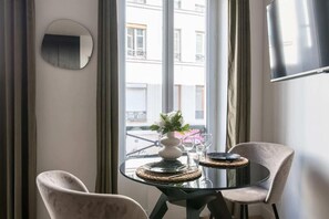 A dining area with a round table, two chairs, a vase with flowers, and a view of buildings outside. - République - Charmant studio - Haystia (Paris)