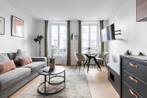 A modern living room with a sofa, coffee table, and a TV mounted on the wall. - République - Charmant studio - Haystia (Paris)