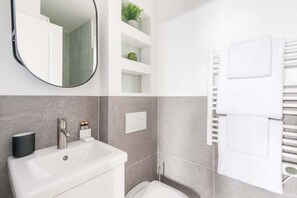A modern bathroom with a white sink, a round mirror, a towel rack, and a toilet. - République - Charmant studio - Haystia (Paris)