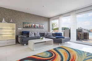 A modern living room with a sectional sofa, a glass cabinet, and a colorful rug. - Holiday apartment with 1 bedroom (Wunstorf Steinhude)