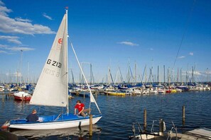 Eine Segelyacht mit weißem Segel mit der Aufschrift 'G 213' liegt in einer Marina mit mehreren Booten festgemacht.