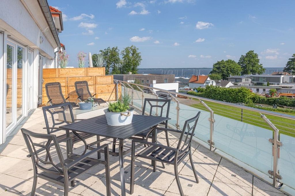 An outdoor patio with a table and chairs, a potted plant, and a view of the sea.