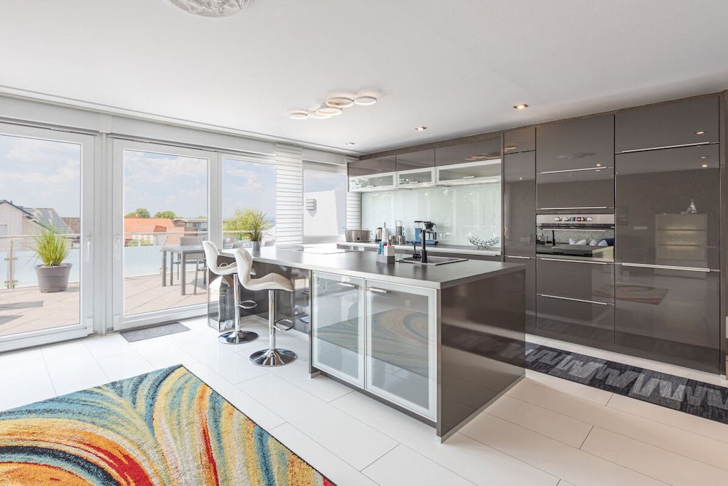 A modern kitchen with a large island, glass cabinets, and a view to the outside.
