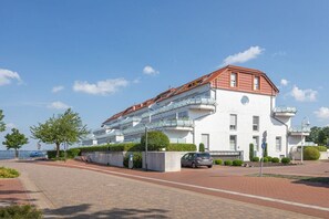 Ein modernes Gebäude mit rotem Dach, großen Fenstern und einer gepflasterten Fläche davor.
