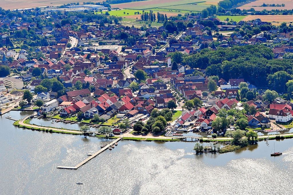 Un quartier résidentiel avec des maisons le long d’une promenade au bord de l’eau, un quai et un pont en arrière-plan.