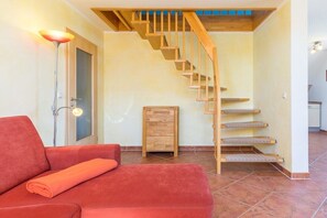 A room with a red sofa, a wooden staircase, and a small wooden cabinet. - B - Holiday home Katharina (Wohlenberg)