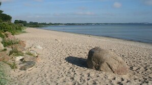 A sandy beach with a large rock in the foreground and a calm body of water in the background. - B - Holiday home Katharina (Wohlenberg)