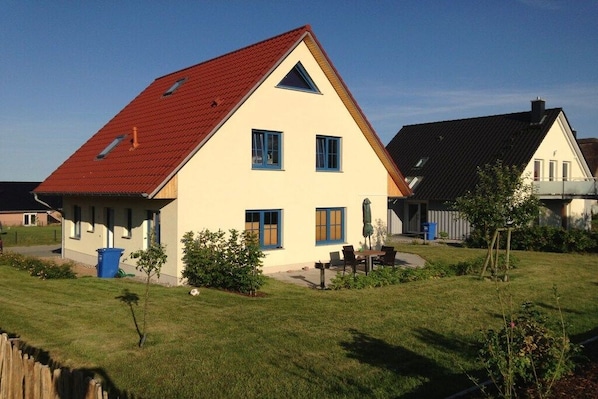 Een woonhuis met een rood dak, een veranda en een verzorgd gazon.