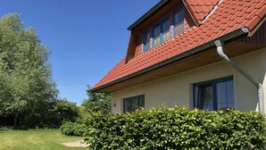 A house with a red-tiled roof, a visible window, and a hedge in the foreground. - B - Holiday home Katharina (Wohlenberg)