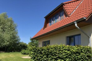Een huis met een rood pannendak, een zichtbaar raam en een haag op de voorgrond.