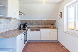 Una cuina compacta amb armaris blancs, un taulell de fusta, un rentaplats integrat i una finestra que deixa entrar llum natural.