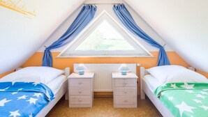 A bedroom with two beds, a window with curtains, bedside lamps, and a radiator. - B - Holiday home Katharina (Wohlenberg)