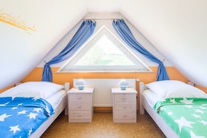 Een slaapkamer met twee bedden, een raam met gordijnen, nachtlampjes en een radiator.
