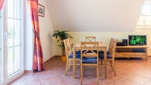 A dining area with a table and chairs, a television, and a potted plant. - B - Holiday home Katharina (Wohlenberg)