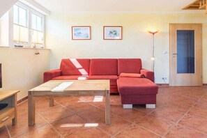 A living room with a red sofa, a wooden coffee table, and two framed pictures on the wall. - B - Holiday home Katharina (Wohlenberg)