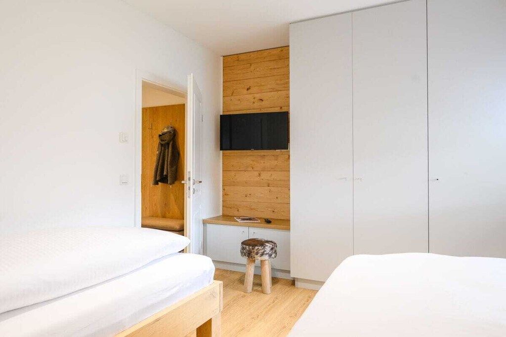 Une chambre avec deux lits, une armoire en bois et un petit tabouret.