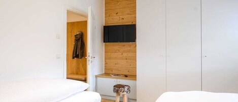 A bedroom with two beds, a wooden wardrobe, and a small stool.