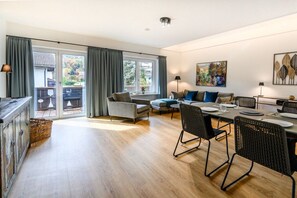 A spacious living area with a dining table, chairs, and a sofa. There is a sliding glass door leading to an outdoor balcony.