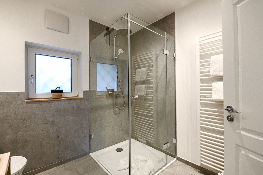 A modern bathroom with a glass-enclosed shower, a towel rack, and a window with a basket.