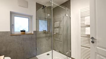 A modern bathroom with a glass-enclosed shower, a towel rack, and a window with a basket.