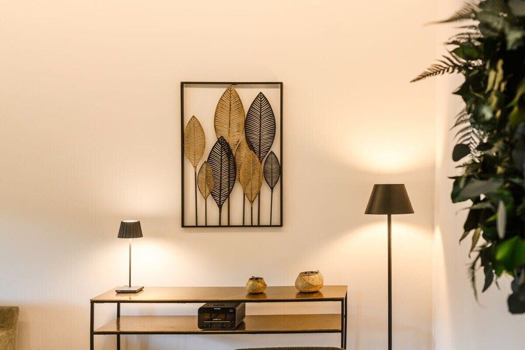 Ein Zimmer mit einem gerahmten Kunstwerk von Blättern, einem Konsolentisch mit einem Radio und zwei Stehlampen.