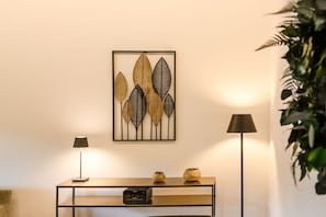 A room with a framed artwork of leaves, a console table with a radio, and two floor lamps.