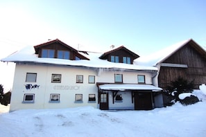 Kaksikerroksinen rakennus, jonka katto on lumen peitossa, ja jossa on pieni, siihen liittyvä lisärakennus.