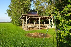 A wooden gazebo with a metal roof, surrounded by lush greenery and a grassy field. - at the Feneberg holiday farm (Eggenthal)