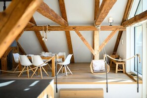 Un coin repas avec une table et des chaises en bois, un fauteuil suspendu et une vue sur l’extérieur.