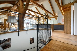A rustic interior with exposed wooden beams, a netted enclosure, and a kitchen area in the background. - Holiday apartment with 2 bedrooms (Garmisch-Partenkirchen)