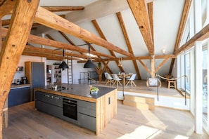 A modern kitchen with a central island, wooden beams, and a dining area with chairs. - Holiday apartment with 2 bedrooms (Garmisch-Partenkirchen)