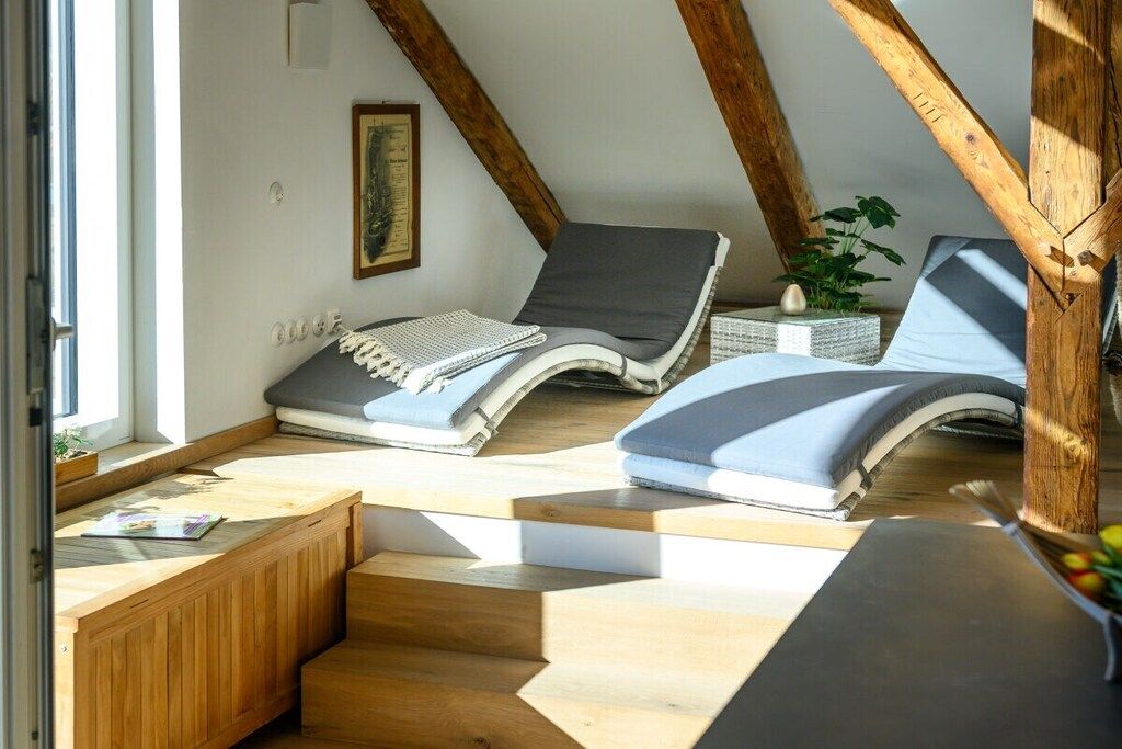 Ein sonnendurchflutetes Zimmer mit schrägen Wänden, einem kleinen Tisch mit einem Notizbuch und zwei bequemen Lounge-Sesseln mit Kissen.