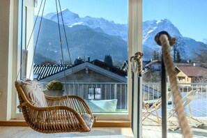A room with a large window overlooking a mountain landscape, a wicker chair, and a hanging chair. - Holiday apartment with 2 bedrooms (Garmisch-Partenkirchen)