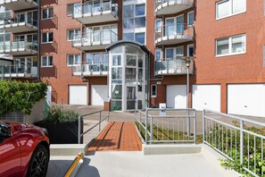 Een meerlaags woongebouw met balkons, een hekpoort en een rode auto ervoor geparkeerd.
