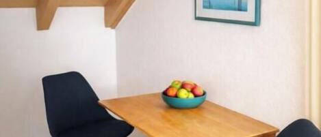 Un comedor con una mesa de madera y dos sillas, un cuenco de fruta sobre la mesa, y un cuadro en la pared.
